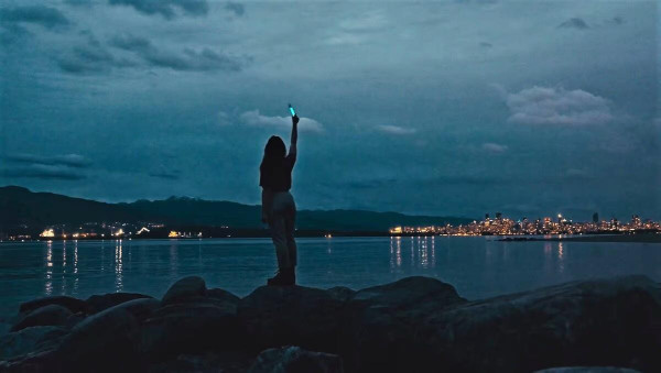 A person holding a glowstick and a city lit up for night in the background.